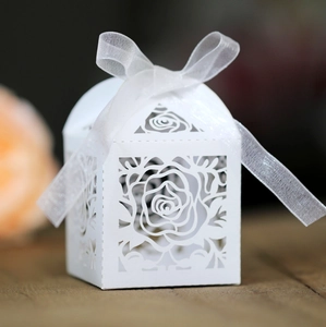 Macro view of laser-cut rose hollow favor box with delicate white silk ribbon bow