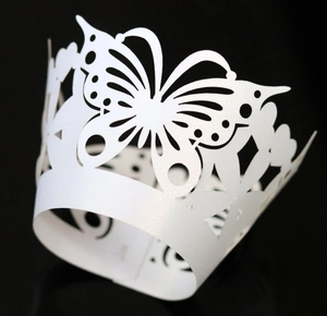 Macro shot of laser-cut white cupcake wrapper with intricate butterfly and crown patterns