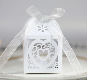 Macro shot of white laser-cut wedding favor box with heart patterns and silk ribbon bow