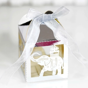 Macro detail of white laser-cut party favor box with silver ribbon and elephant pattern