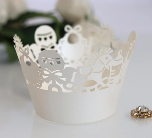 Detail of cream laser cut cupcake wrapper with baby shower bottle and rattle patterns