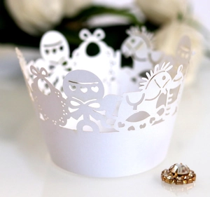 Laser-cut white cupcake wrappers with baby shower patterns like rocking horses and bibs
