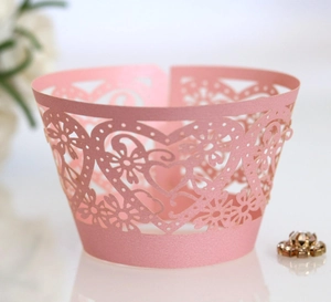 Pink laser-cut paper cupcake wrappers with heart and floral patterns for wedding decor