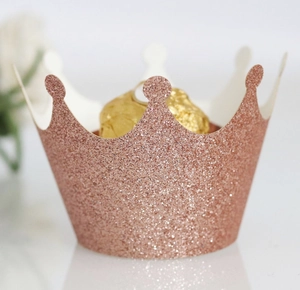 Detail of rose gold glitter cupcake wrapper with hollow crown design and chocolates
