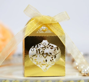 Macro detail of golden laser-cut heart favor box with yellow organza bow and vine pattern