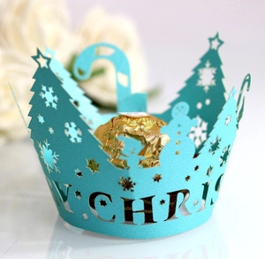 Close-up of laser-cut teal Christmas cupcake wrapper with festive tree and snowflake motifs
