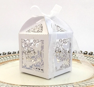 Close-up of laser-cut butterfly wedding favor box with white organza ribbon on porcelain plate