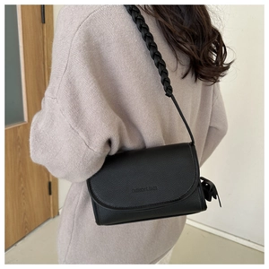 Detail of a black textured crossbody bag with thick woven shoulder strap and side tassel