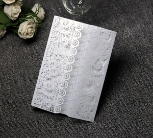 Detail of white laser-cut floral lace wedding invitation on grey textured background