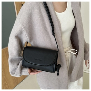 Detail of black pebbled leather crossbody bag with braided strap and puppy charm