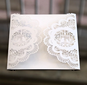 Detail of laser-cut white pearlescent paper invitation with elegant bird and lace patterns