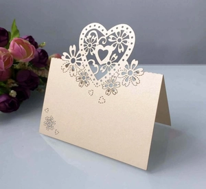 Dettaglio segnaposto crema intagliato al laser con cuore e decorazioni floreali per matrimoni