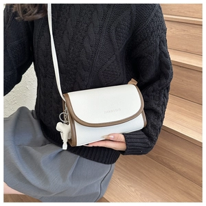 Close-up of white pebble leather crossbody bag with brown trim and elephant charm