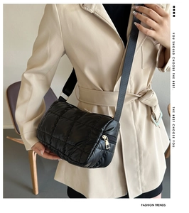 Close-up of black quilted down shoulder bag with glossy texture and wide nylon strap