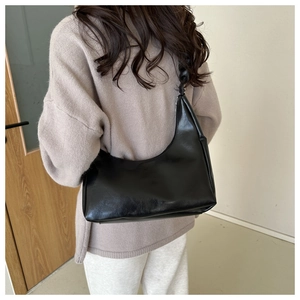 Detail view of black pleated underarm bag featuring a unique knotted handle design on a model