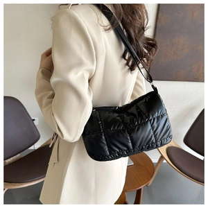 Detailed view of black quilted glossy nylon shoulder bag worn by model in casual setting