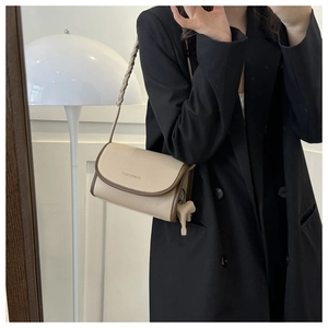 Detail of beige lychee textured crossbody bag with brown trim and woven handle strap