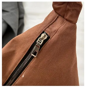 Detail of smooth metal zipper and knot handle design on a brown canvas crossbody bag
