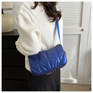 Blue quilted puffer bag worn as crossbody showing soft texture and glossy finish
