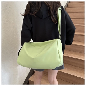 Detail of light green large capacity oxford crossbody bag worn by a model on a shoulder