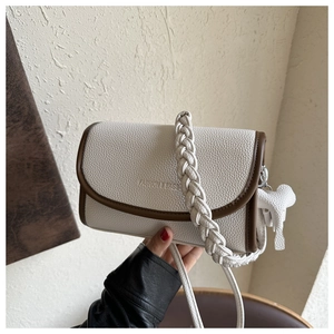 Detail of cream-white lychee texture bag with brown trim and woven handle and bear charm