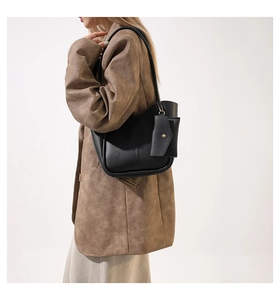 Detail view of a black matte leather tote bag with a small envelope charm on a model