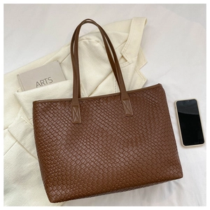 Détail de la texture en cuir tressé marron foncé sur un grand sac cabas pour femmes
