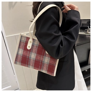 Detail of plaid tote bag with beige leather trim and golden rivets shown on model