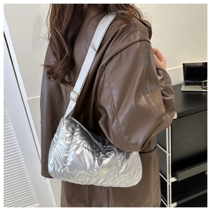 Detail of silver quilted puffer bag showing glossy metallic texture and wide nylon strap