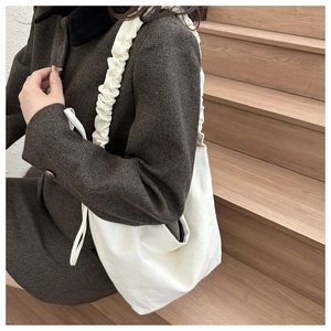 Detail showing the widened ruched shoulder strap on a cream canvas dumpling crossbody bag