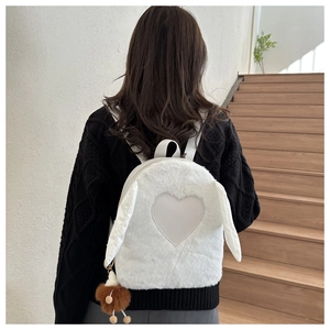 Detail of plush white backpack with bunny ears and heart patch worn by a model