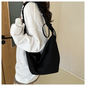 Detail of black canvas shoulder bag with pleated ruffle strap and drawstring knot detail