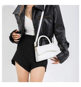 White minimalist crossbody bag with scalloped flap edges worn by model on shoulder