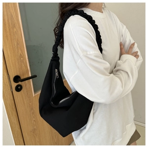 Detailed view of black canvas crossbody bag with pleated shoulder strap and silver zipper