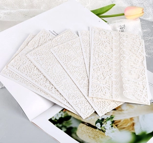 Elegant laser cut lace wedding invitation covers in off-white on a magazine backdrop