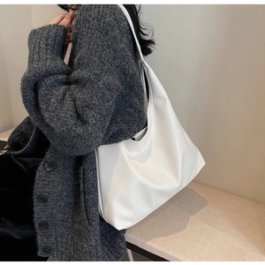 Detailed view of a white large capacity tote bag worn on a woman's shoulder in soft light