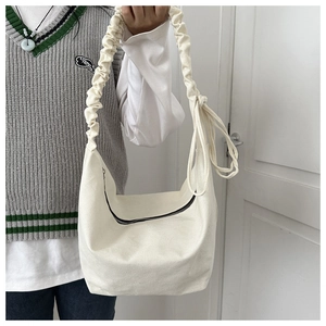 Detail of off-white canvas crossbody bag featuring pleated cloud strap and zipper closure