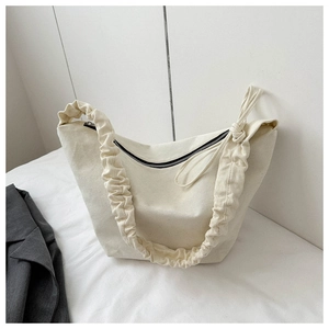 Detail shot of beige canvas tote bag featuring ruffled shoulder straps and black zipper closure
