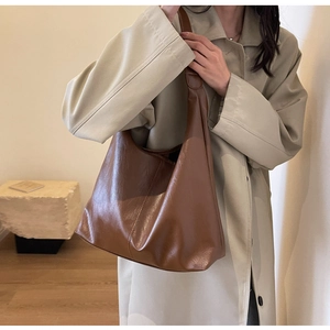 Brown faux leather hobo tote bag with wide strap styled on a beige trench coat
