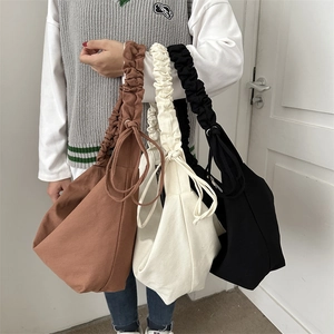 Three minimalist canvas dumpling bags in brown, beige, and black with bow drawstrings