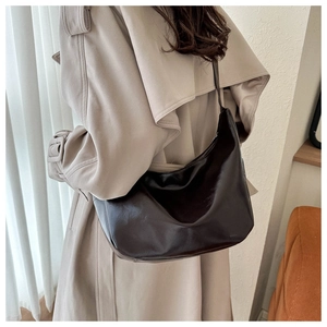 Detailed texture of dark brown polished leather hobo bag worn with a beige trench coat