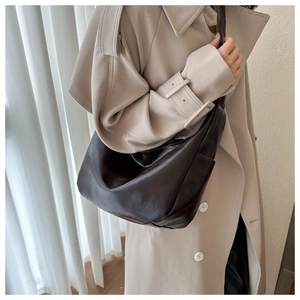Deep brown oversized leather tote bag worn by model in soft indoor window lighting