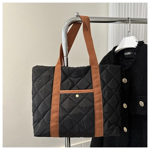 Detail of black quilted tote bag with brown straps and a small gold buckle front pocket