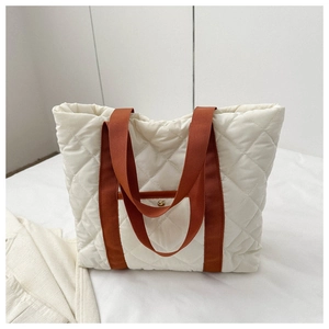 Close-up of quilted white tote bag with orange brown handles and gold snap button