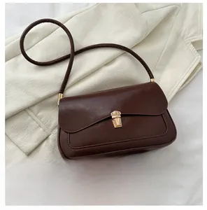Detail of dark brown faux leather crossbody bag with golden clasp and smooth oil-wax texture