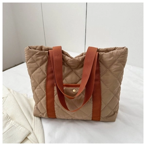 Detail of quilted tote bag with brown fabric, orange handles, and golden snap button