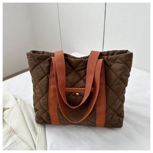 Detail of diamond quilted tote bag featuring orange handles and a gold metal button