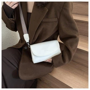 Detail van witte leren crossbodytas met brede geometrische geweven schouderband