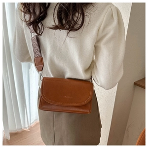 Detailopname van bruine vintage crossbodytas met brede visgraatriem en klepsluiting