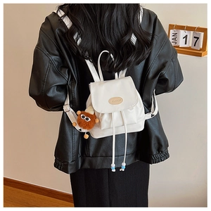 Rear view of a white mini leather backpack featuring a plush monster charm on a black outfit
